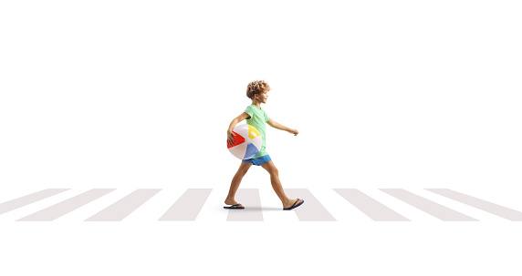 Full length profile shot of a boy walking and carrying a beach ball at a pedestrian crossing