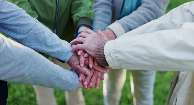 Elderly people, hands together and teamwork for community, trust or support together in nature. Mature or retired group piling in team building, collaboration or friends in motivation at outdoor park