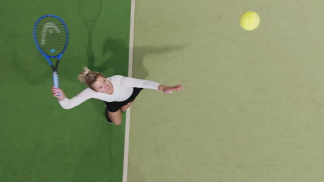 SLO MO SPEED RAMP Directly Above Shot of Young Female Tennis Player Serving Ball on Court in Sports Club