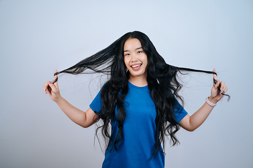 Portrait of young Asian woman lifting long shiny curly hair on white background in studio,Hair styling.