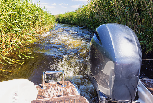 Motor boat sailing on a water canal from the Curonian Lagoon among reeds, Lithuania 2021. 20. 20.