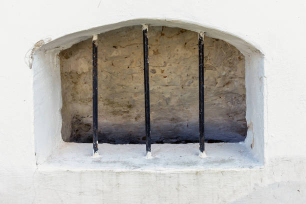 The basement window of the old building is covered with metal bars and walled in from the inside