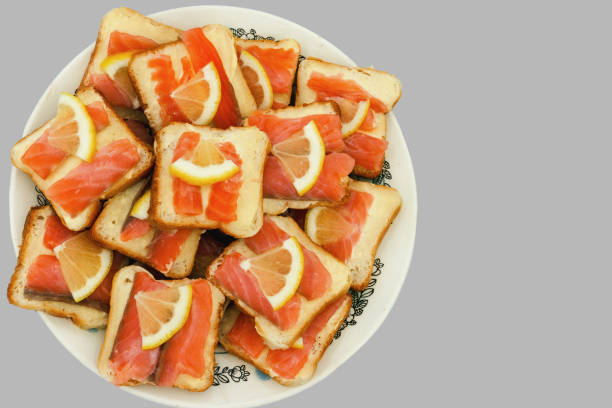 Snacks with smoked salmon and white bread smeared with butter, topped with a slice of lemon