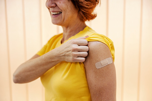 A happy middle-aged woman showing a shoulder after a shot of seasonal flu vaccine.