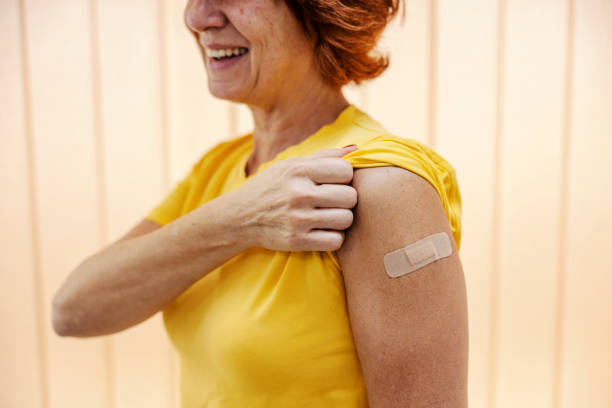 счастливая женщина средних лет показывает плечо после укола вакцины от сезонного гриппа в больнице. - injecting flu virus cold and flu doctors office стоковые фото и изображения