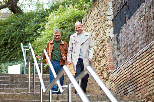 Full length view of mature men in casual attire, side by side and moving down urban staircase, enjoying each other’s company.