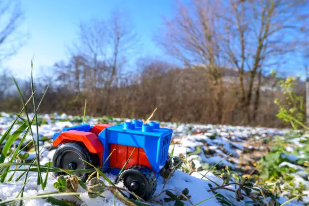 Plastic toy tractor red and blue in agriculture on snowy field in Germany