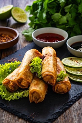 Spring rolls filled with meat and vegetables served with soy sauce on wooden table