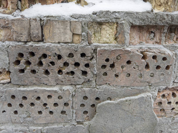 Fragment of the old rough partly destroyed wall made with cracked red bricks covered with hoarfrost and snow, outdoors in overcast day