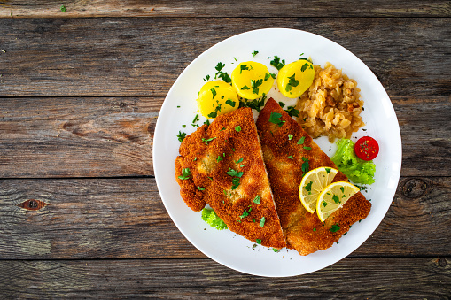 slices of smoked salmon, decorated with herbs, onion and lemon, with salad and a sidedish of fried potatoe pancakes, ,served on a white plate