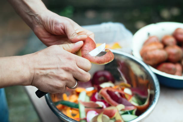 close up of a man peeling vegetables and making compost from leftovers at an open kitchen outdoors at back yard. sustainable lifestyle and zero waste cooking concept. - carrot close up copy space counter top ストックフォトと画像