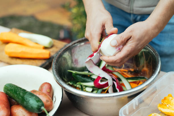 Close up of a man peeling vegetables and making compost from leftovers at an open kitchen outdoors at back yard. Sustainable lifestyle and zero waste cooking concept.