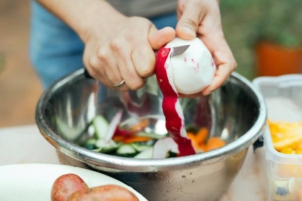 close up of a man peeling vegetables and making compost from leftovers at an open kitchen outdoors at back yard. sustainable lifestyle and zero waste cooking concept. - carrot close up copy space counter top ストックフォトと画像