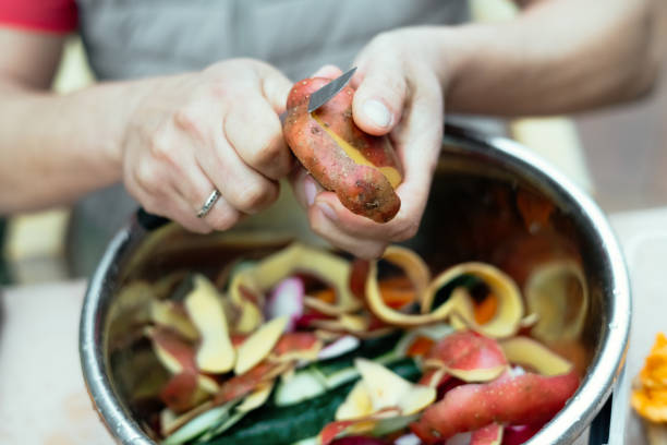 close up of a man peeling vegetables and making compost from leftovers at an open kitchen outdoors at back yard. sustainable lifestyle and zero waste cooking concept. - carrot close up copy space counter top ストックフォトと画像