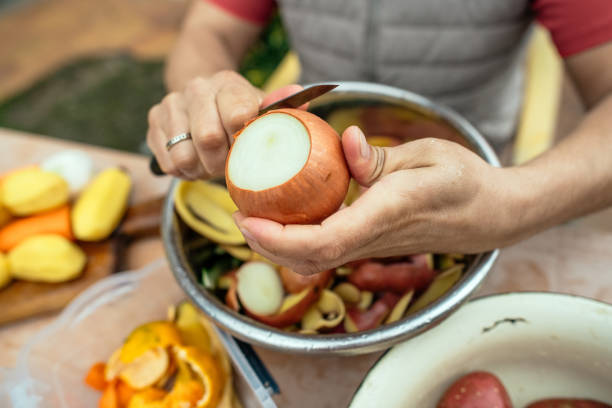 close up of a man peeling vegetables and making compost from leftovers at an open kitchen outdoors at back yard. sustainable lifestyle and zero waste cooking concept. - carrot close up copy space counter top ストックフォトと画像