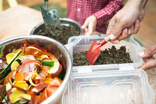 Family making compost from leftovers at an open kitchen outdoors at back yard. Father teaches his child to grow organic plants. Sustainable lifestyle and zero waste cooking concept.