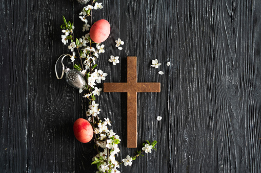 Spring cherry blossoms and Easter eggs and cross on old wooden background. Easter is a Christian holiday