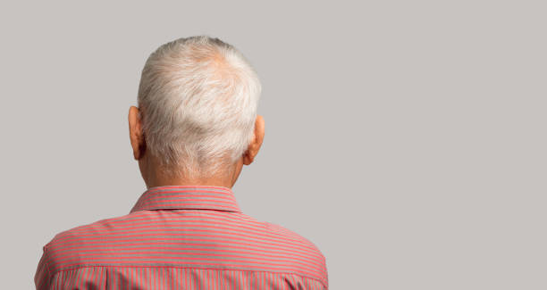 istock Back view of a senior man with short gray hair while standing on a gray background 1942005451