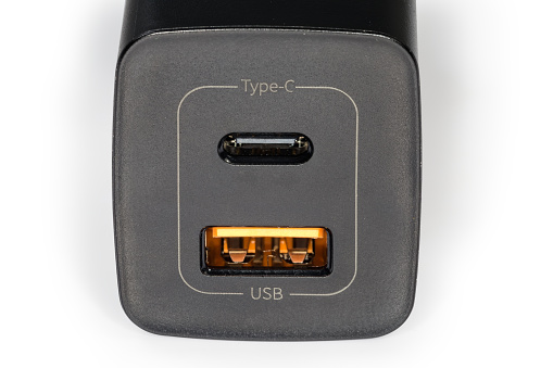 Front panel of the black charger with two USB Type-A and Type-C output sockets for batteries charging of portable accessories, fragment close-up on a white background