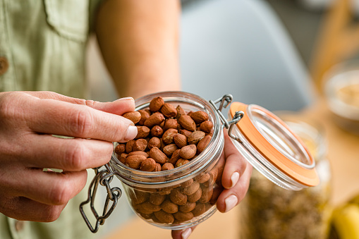 Close up of woman's hands taking organic unshelled peanuts from glass jar. High resolution 42Mp studio digital capture taken with Sony A7rII and Sony FE 90mm f2.8 macro G OSS lens