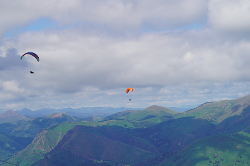 Two paragliders fly over the Pyrenees mountains, in the Basque Country