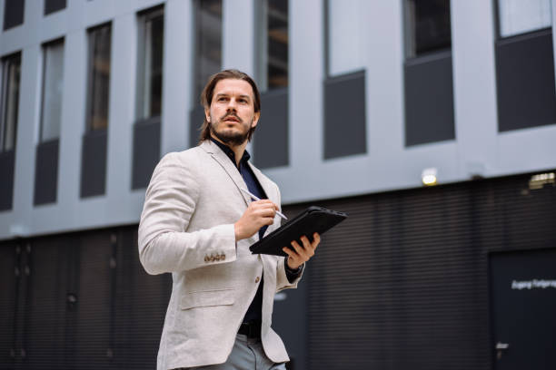 istock Professional employee writing notes on tablet while standing near the office building 1942087124