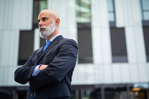 Portrait of a senior confident businessman with shaven head and white beard in a modern city