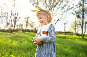 Small girl wearing Bunny ears laughing cheerfully against the background of a blooming garden on Easter Day. Celebration in the open air. Happy Child