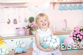 Cute little girl with bunny ears holding Easter egg in the kitchen decorated for Easter.