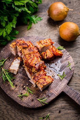 Grilled pork belly with crispy skin, with onion and herbs  on wooden background