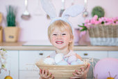 Little girl holds a basket with painted Easter eggs. Happy child in the bright kitchen at home on Easter