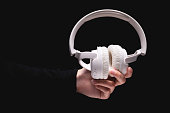 woman hand holds large white headphones on a black background. A girl holds out wireless headphones to the camera, close-up