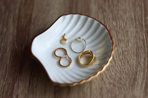Ring dish shaped like a seashell with gold rings, earrings and pendant. Wooden background, selective focus.