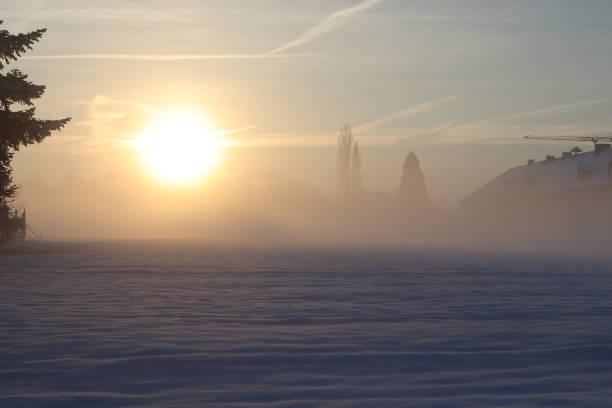 A sunrise during a cold winter morning with snow and mist, a farm and trees barely visible.