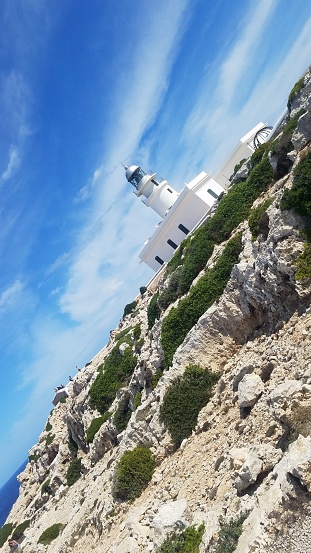 Perched high on a rocky hill, a white building stands tall against the expansive outdoor landscape, its sharp lines contrasting against the softness of the sky and clouds above