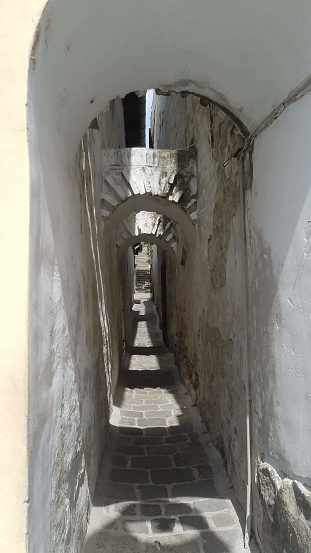 The shadowed alley, with its narrow walls of concrete, stood between towering buildings, creating an outdoor pathway that seemed to lead to a hidden world beneath the ground