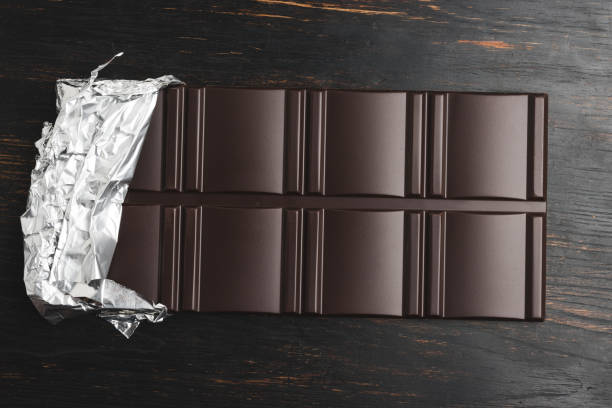 Delicious dark chocolate bar wrapped in foil on a dark wooden background, top view