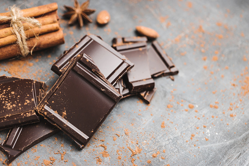 Heap of delicious dark chocolate pieces or cubes, chopped, broken chocolate bar, almond nut, cinnamon sticks and star anise on a dark background.