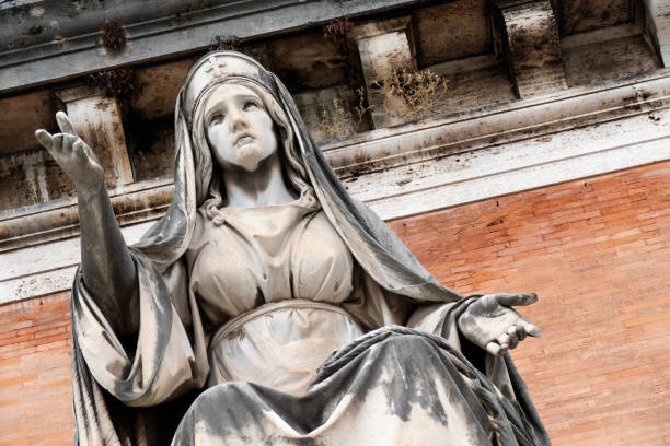 A beautiful marble statue of a woman holding a vessel, set against a bright sky with sunlight shining through the trees behind her. The statue exhibits intricate details and a serene expression.