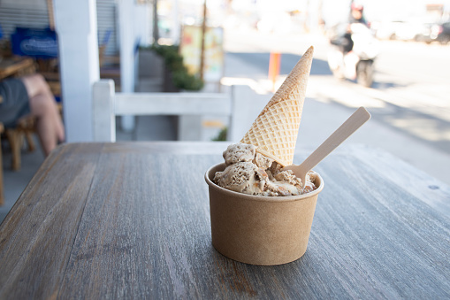ice cream shop with delicious pot of artisanal dulce leche ice cream with cone on wooden table on sunny day with sustainable wooden spoon