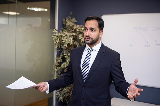 Business executive making a presentation in front of a whiteboard in a boardroom. He is formally dressed in a suit, shirt and tie.