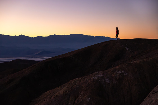 Alone tourist stands on weathered rocks, gazing at distant mountains under a mesmerizing sunset sky. The isolation amidst nature's grandeur captures the essence of this serene moment