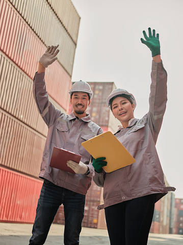 A team of engineers waving hand to say hello, greeting someone at the Container cargo . Quality inspection, work plan,  industrial building design project