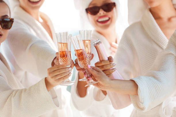 female friends in white bathrobes before a bachelorette party toasting with champagne - addio al nubilato foto e immagini stock