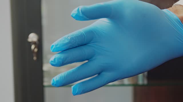 A male doctor puts on blue and rubber protective gloves. Close-up