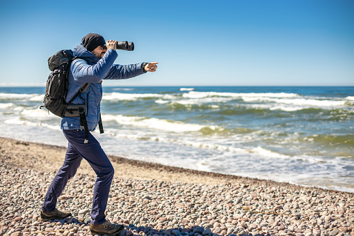 A tourist man on the seashore, looking through binoculars, pointing his finger to something