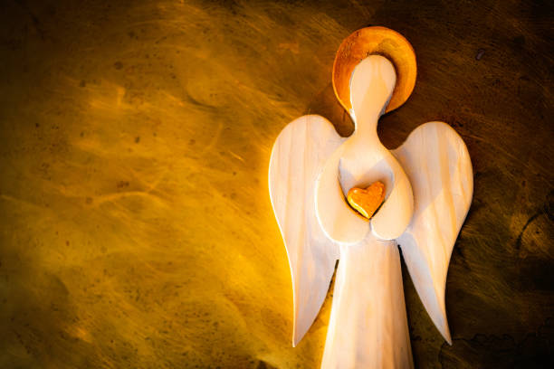 A wooden figure of an Angel with a golden halo. Golden heart. A wooden figure of an Angel with a golden halo. Golden heart. Burning background imitation. Grainy photo. church like a holy light from god stock pictures, royalty-free photos & images