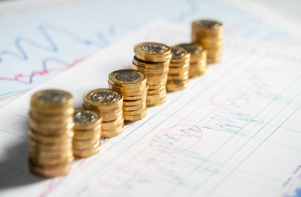 stack of pound coins on financial graphs and figures - british currency pound symbol currency stack foto e immagini stock