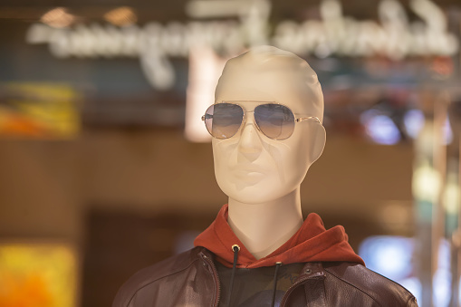The face of a male mannequin in sunglasses behind the glass of a display case.