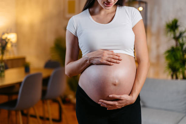 young pregnant woman standing in the living room at night - ciąża zdjęcia i obrazy z banku zdjęć
